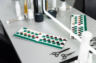kuaför aletleri, kuaför makasları, şişeler, saç yağı, tarak, yuvarlak fırça, kuaför salonundaki aynanın yanındaki saç paleti kitabı, kuaför malzemeleri, güzellik endüstrisi, saç modası 