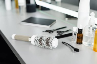 Salon aksesuarları, yuvarlak fırça ve profesyonel kuaför tokasına odaklan, saç kesme aletleri, kuaför makasları, şişeler, kuaför salonundaki aynanın yanındaki saç yağı, güzellik endüstrisi 