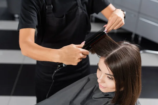 stock image top view of professional hairdresser with hair straightener styling hair of female customer, beauty worker, client satisfaction, brunette woman with short hair, beauty salon, hair fashion 