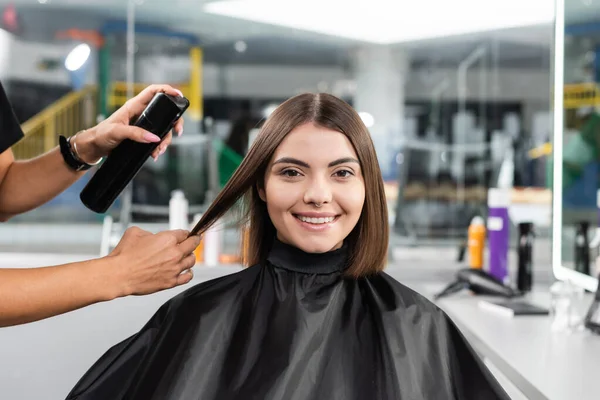 salon services, hair spray, hairdresser styling hair of female customer with nose piercing, happy brunette woman with short hair, beauty salon, hair volume, hair professional, hairdressing cape