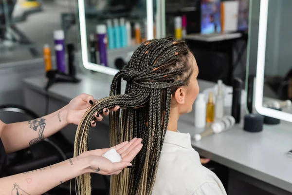 beauty industry, hair product, tattooed hairdresser with styling foam in hand, woman with braids in salon, beauty worker, salon customer, beauty worker, hair professional, client satisfaction