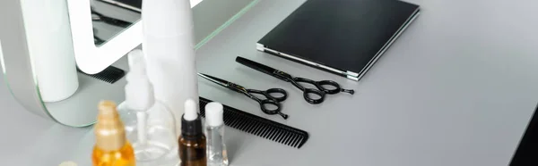 hairstyling products, hairdressing scissors, bottles, hair oil, comb, hair palette book near mirror in beauty salon, hair essentials, beauty industry, hair fashion, hair industry, banner
