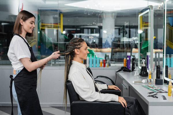 side view, client satisfaction, hairdresser styling hair of female customer, looking at mirror, happy woman with braids, hairstyle, braided hair, beauty salon, hairstyling products 