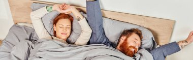 quiet house, parents alone at home, redhead husband and wife in cozy bedroom, bearded man and carefree woman relaxing on weekends, day off, wake up, tattooed, closed eyes, enjoy, top view, banner  clipart