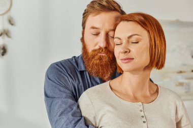 married couple hugging in cozy bedroom, day off without kids, redhead husband and wife, enjoying time together, weekends together, tattooed, love and bonding, parents alone at home clipart
