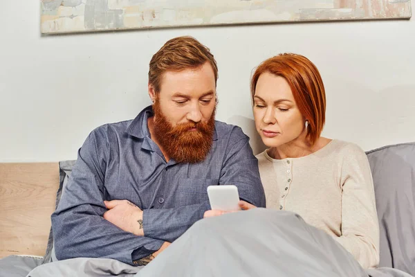 数码情侣 银幕时间 周末休息没有孩子 丈夫和妻子 留着胡子的男人和红头发的女人使用智能手机 舒适的卧室 一天休息 — 图库照片