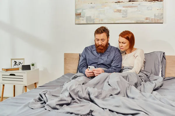 数码情侣 屏幕时间 周末放松没有孩子 丈夫和妻子 留着胡子的男人和红头发的女人使用智能手机 舒适的卧室 一天的休息 纹身夫妇 — 图库照片