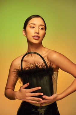 fashion choices, brunette asian woman with bare shoulders posing with feather purse on green background, gradient, fashion forward, glowing skin, natural beauty, young model  clipart