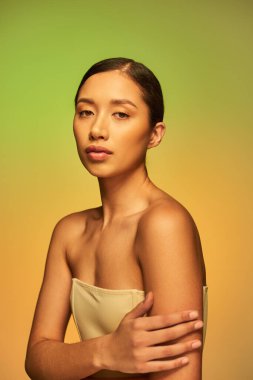 asian beauty, young woman with brunette hair and bare shoulders posing on gradient background, green and orange, skin care, glowing skin, natural beauty,  beauty model  clipart