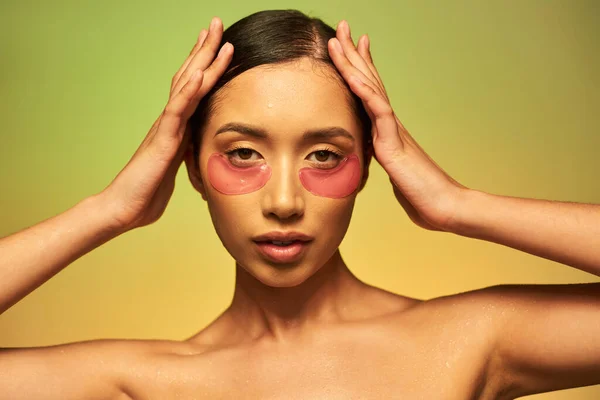 护肤活动 年轻的亚洲女人 一头乌黑的头发和洁白的皮肤 双手贴在绿色的背景上 赤裸的肩膀 润肤的眼斑 发亮的皮肤 — 图库照片