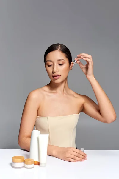 美容キャンペーン スキンケア ブロンドの髪を持つ若いアジアの女性は 灰色の背景にピペットと血清を適用します 輝くと健康肌 顔の治療の概念 美容製品 — ストック写真