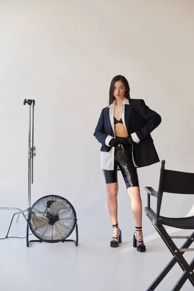 时尚前卫 工作室摄影 年轻的亚洲女人穿着灰色背景 白色衬衫和乳胶短裤 站在电扇边 — 图库照片