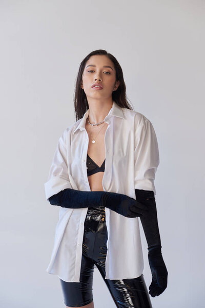 beauty and fashion, bold style, young asian woman posing on grey background, model looking at camera, black gloves and white shirt, bra look, fashion statement, conceptual, personal style