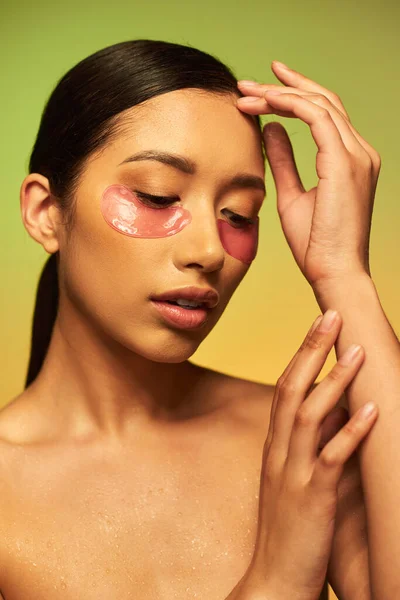 pretty and brunette asian woman posing with eye patches on green background, gradient, beauty, skin perfection, facial treatment, bare shoulders, skincare routine, glowing skin, portrait