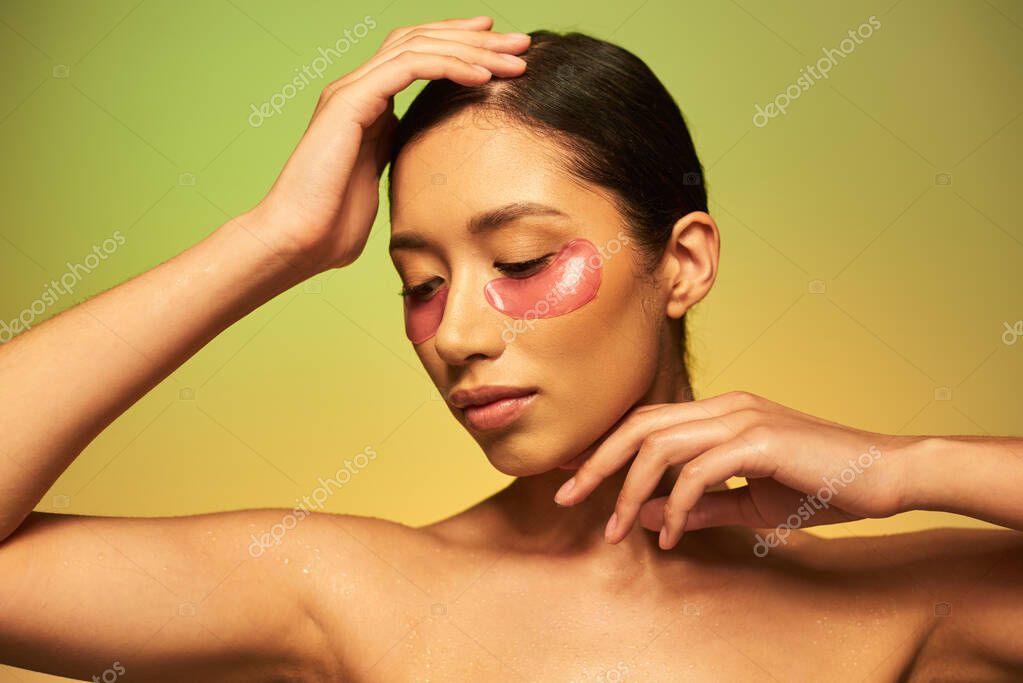 Beauty campaign, young asian woman with brunette hair and clean skin posing with hands near face on green background, bare shoulders, moisturizing eye patches, glowing skin
