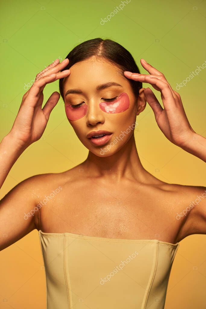 Beauty model, glowing skin, young asian woman with brunette hair and clean skin posing and looking down on green background, bare shoulders, moisturizing eye patches, skincare product