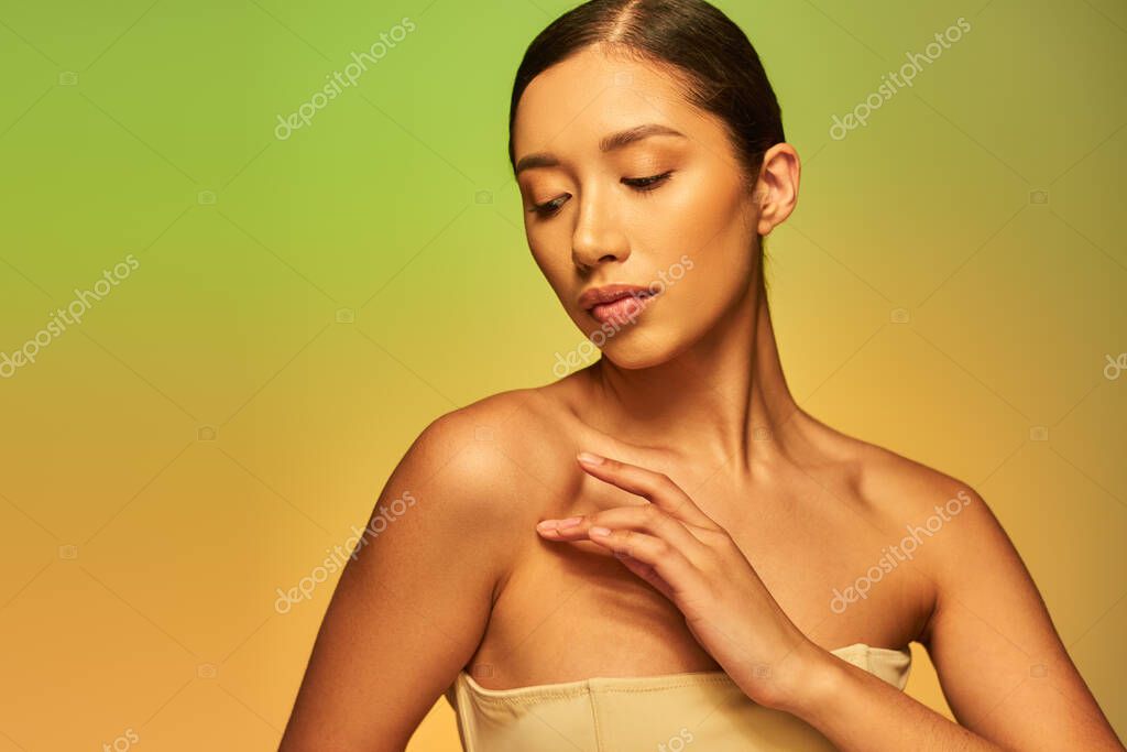 Skin care and beauty, asian woman with brunette hair and bare shoulders posing on gradient background, green and orange, skin care, glowing skin, natural beauty, young model