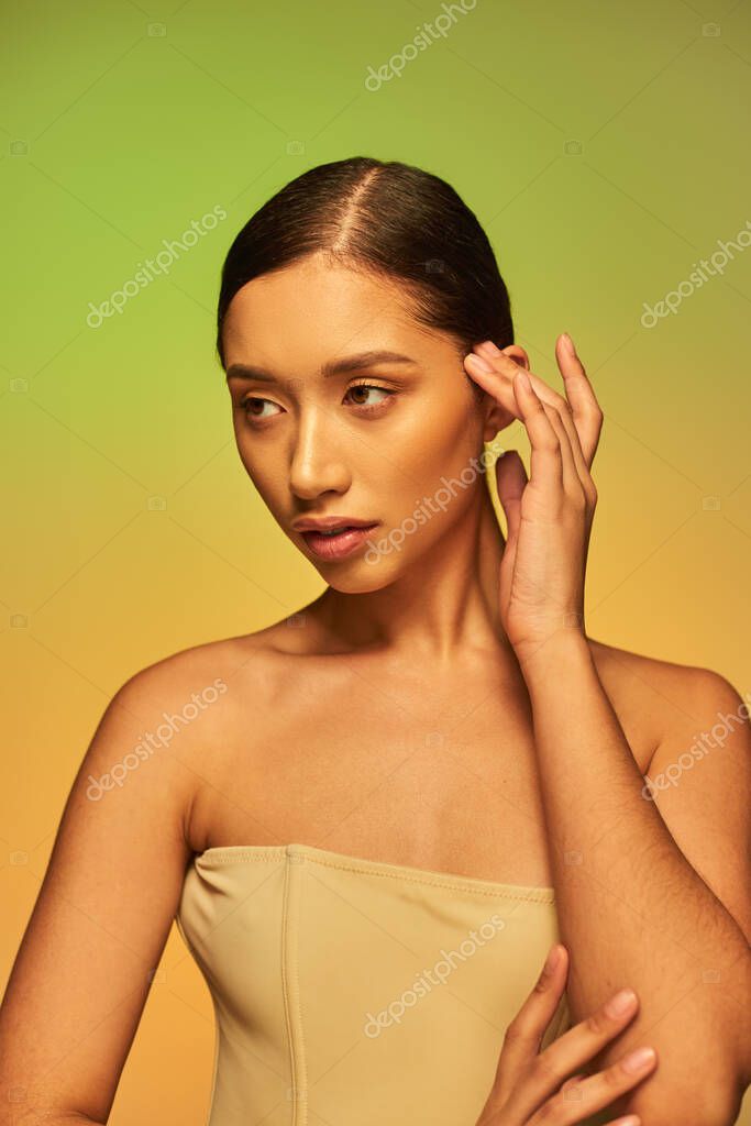 Beauty photography, attractive asian woman with brunette hair and bare shoulders posing on gradient background, green and orange, skin care, glowing skin, natural beauty, young model