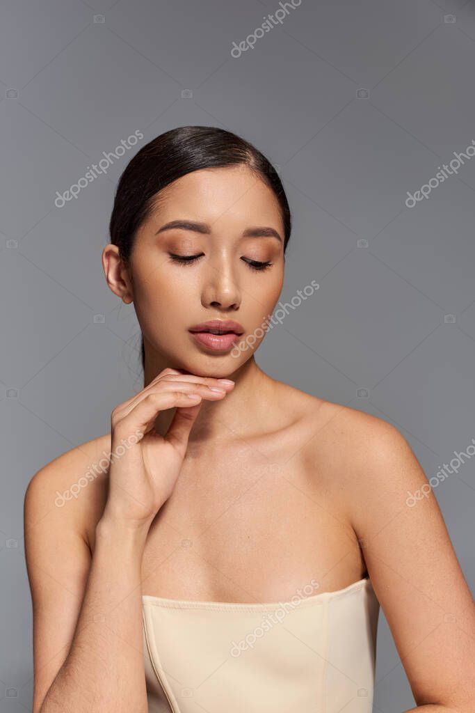 Sensuality, pretty asian woman with brunette hair and bare shoulders posing on grey background, skin care, healthy skin, natural beauty, young model, clean and glowing skin