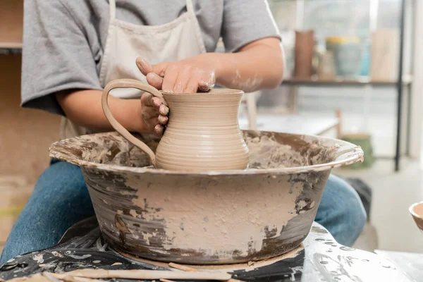 青銅製の若い女性職人がテーブルの上にテーブルの上に陶器の車輪で作業しながら 粘土のジャグを作るエプロンのビューをトリミングセラミックワークショップ 職人の陶器の生産とプロセス — ストック写真
