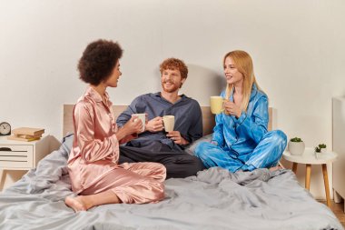 love triangle, polygamy, redhead man and interracial women in pajamas holding cups of coffee, morning routine, bisexual, understanding, three adults, cultural diversity, acceptance  clipart