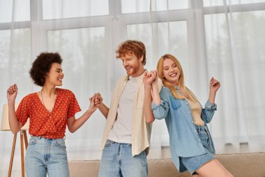 polygamy, happy multicultural women and bearded man holding hands, having fun, dancing in living room, love and diversity in relationships, modern family, acceptance and bonding  clipart