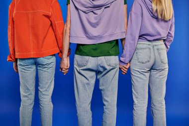 polygamy, back view of polyamory three people, young man and women holding hands on blue background, studio shot, vibrant clothes, love triangle, cropped shot, bonding, alternative relationships clipart
