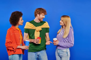 alternative relationships, polyamory lovers with coffee, young redhead man and beautiful multiracial women holding paper cups on blue background, studio shot, takeaway drink, polygamy people clipart