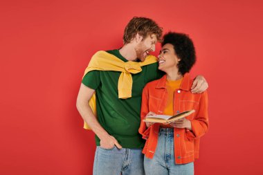 Mercan arka planı, kültürel çeşitlilik, canlı renkler, şık kıyafetler, gençlik ve zeka üzerine kucaklaşıp kitap okuyan ırklar arası bir çift.