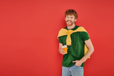 morning coffee, redhead man with beard and curly hair holding paper cup on coral background, vibrant colors, male fashion, takeaway drink, happy and stylish man posing with hand in pocket  clipart