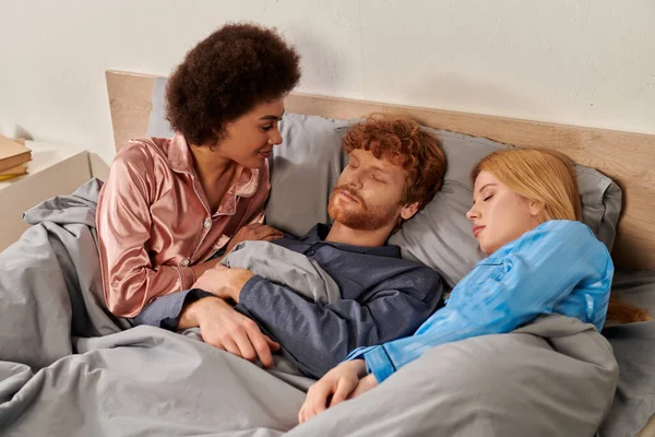 爱情三角 觉醒的非洲女人美国女人看着红头发男人接近金发女性伴侣在床上 一夫多妻制 非传统的关系 多种族 文化多样性 — 图库照片