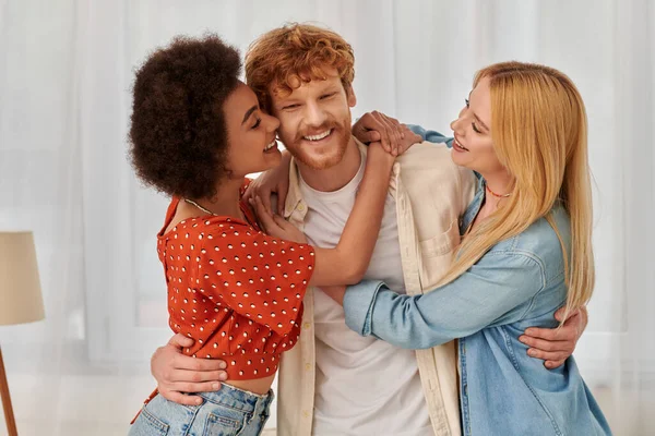 non traditional relationship, polygamy, three adults, happy interracial women hugging redhead man, threesome, cultural diversity, acceptance, bonding and love, multiracial lovers