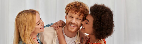 non traditional family, polygamy, three adults, happy interracial women hugging redhead man, threesome, cultural diversity, acceptance, bonding and love, multiracial lovers, banner