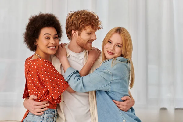 stock image portrait of non traditional lovers, polygamy, three adults, happy redhead man hugging with multicultural women, threesome, cultural diversity, acceptance, bonding and love, multiracial lovers 