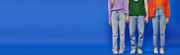 代替関係 一夫多妻制 ポリアモリーの部分的なビュー3人 青の背景に手を握って若い男と女性 スタジオショット 活気のある服 現代の愛の三角形 バナー — ストック写真