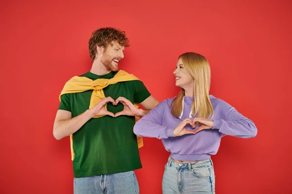 stock image young couple looking at each other on coral background, showing heart sign with hands vibrant colors, stylish outfits, modern family, handsome man and beautiful woman, bonding and love, togetherness 