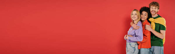 polygamy concept, three interracial lovers hugging on coral background, cultural diversity, polyamorous, happy multiethnic people looking at camera, casual attire, open relationship, banner