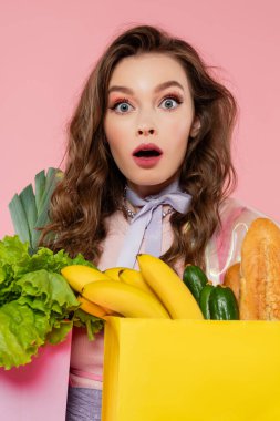 housewife concept, shocked woman carrying grocery bags with vegetables and bananas, model with wavy hair on pink background, conceptual photography, home duties, emotional, portrait  clipart