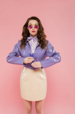 doll pose, beautiful young woman in sunglasses holding soda can and looking at camera, trendy outfit, brunette model in purple jacket posing on pink background, studio shot, carbonated drink,  clipart