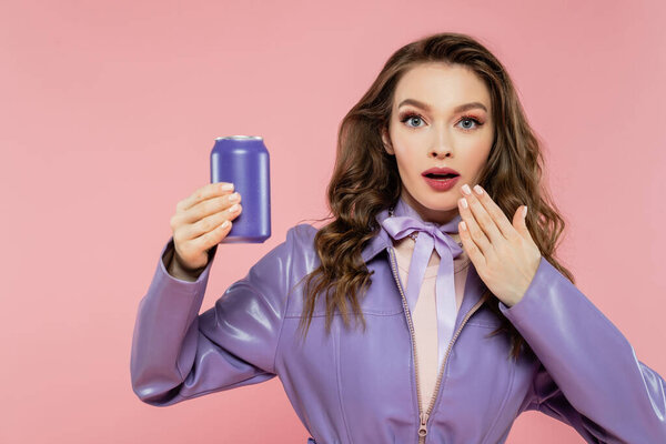 doll pose, shocked young woman holding soda can and looking at camera, hand near mouth, trendy outfit, brunette model in purple jacket posing on pink background, studio shot, carbonated drink 
