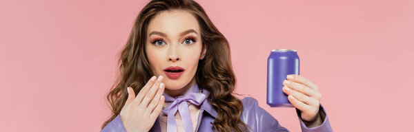 doll pose, astonished young woman holding soda can and looking at camera, hand near mouth, trendy brunette model in purple jacket posing on pink background, studio shot, carbonated drink, banner 