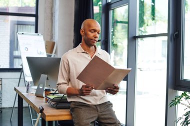 dark skinned man with myasthenia gravis disease holding folder and standing near desk and walking cane, bold african american office worker with ptosis eye syndrome, inclusion, monitor and graphics  clipart