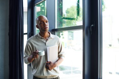 african american man with myasthenia gravis disease holding folder and cup of coffee, bold and dark skinned office worker with ptosis eye syndrome, inclusion, standing near windows   clipart