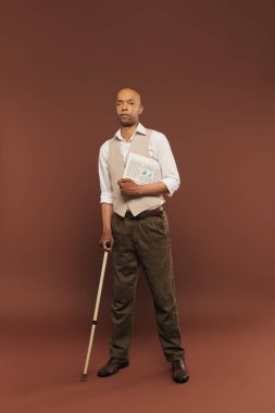 Myasthenia Gravis sendromlu cesur Afro-Amerikan erkeği, elinde gazete ve bastonla, kahverengi arka planda kronik hastalığı olan esmer tenli bir adam.