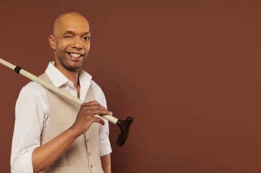 Kapsama, miastenia gravis sendromu, neşeli Afrikalı Amerikalı adam baston tutuyor, kameraya bakıyor, koyu tenli, pozitiflik, nörolojik bozukluk, fiziksel bozukluk. 