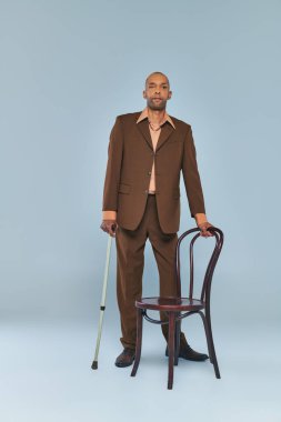 Ptosis sendromu, koyu renkli, baston, çeşitlilik ve kapsamı olan takım elbiseli, gri arka planda sandalyenin yanında duran koyu renkli, miastenya gravis 'li cesur Afrikalı Amerikalı adam. 