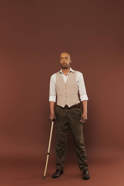 real people, bold african american man with myasthenia gravis syndrome standing with walking cane on brown background, standing and looking at camera, diversity and inclusion, physical impairment 