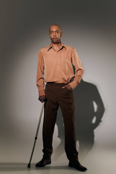 real people, bold african american man with myasthenia gravis standing with walking cane on grey background, hand in pocket, pose, dark skinned person in shirt, diversity and inclusion, full length 