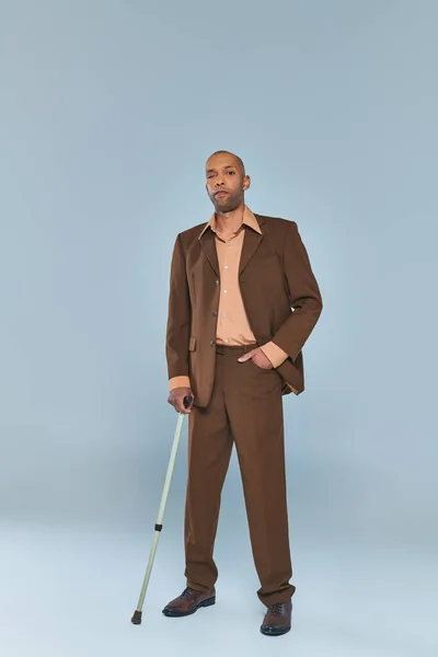 ptosis syndrome, full length of bold african american man with myasthenia gravis standing on grey background, dark skinned person in formal wear holding walking cane, diversity and inclusion