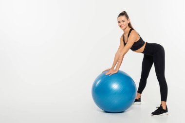 brunette sportswoman looking at camera while standing near fitness ball on white background  clipart
